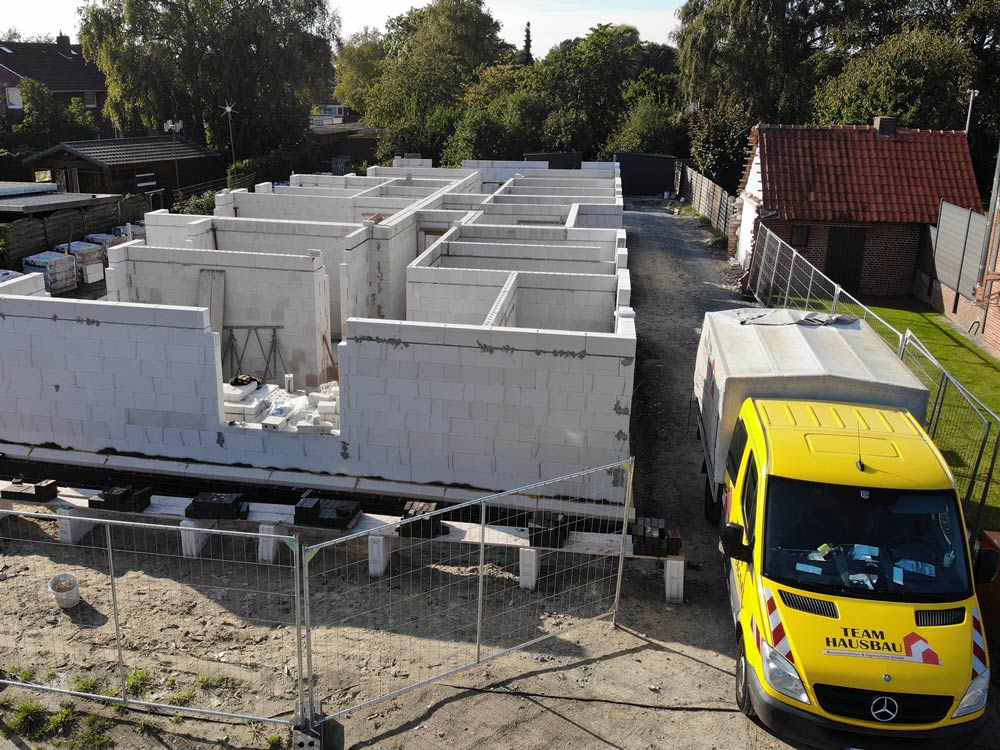 Baustelle mit Rohbau aus weißen Mauersteinen und gelbem Transporter mit Aufschrift 'TEAM HAUSBAU'